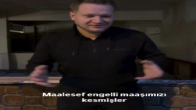 Kapalı bir mekânda ayakta duran bir adam, ellerini kullanarak bir şeyi anlatır gibi konuşuyor. Üzerinde siyah kıyafetler var. Görüntünün alt kısmında “Maalesef engelli maaşımızı kesmişler” yazısı yer alıyor. Sahne, yaşadığı bir mağduriyeti dile getirdiği bir anı yansıtıyor.