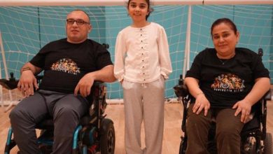 Aylin ve Ahmet Arslan çifti, spor salonunda tekerlekli sandalyede bulunuyor ve kızları ortada durarak poz veriyorlar.