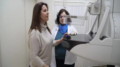 Bir sağlık merkezinde, bir kadın mamografi cihazında tarama için pozisyon alırken, yanında sağlık personeli süreci dikkatle takip ediyor.