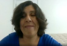 Mavi bluzlu, dalgalı kısa saçlı bir kadın, sade beyaz bir arka plan önünde gülümseyerek konuşuyor. Bir video görüşmesinden alınmış, yakın çekim bir kare.