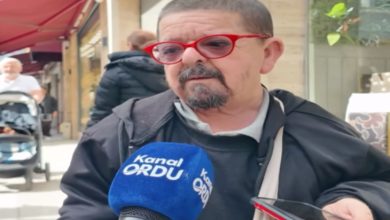 Sokakta yapılan bir röportajda, kırmızı çerçeveli gözlük takan bir adam mikrofonlara konuşuyor. Önünde “Kanal Ordu” yazılı bir mikrofon tutulurken, yanında bir telefon da kayıtta. Arka planda kafe ve yaya trafiği görülüyor; sahne gündelik bir sokak röportajını yansıtıyor.