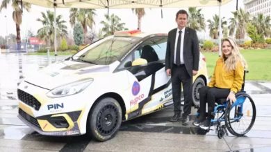 Görselde, engelli ralli pilotu Kübra Denizci Keskin ile Osmangazi Belediye Başkanı Erkan Aydın yan yana görülüyor. Keskin, tekerlekli sandalyesinde otururken kamera karşısına gülümseyerek poz veriyor. Yanlarında, yarışlar için hazırlanmış sponsorluk logoları taşıyan bir ralli aracı bulunuyor. Araç, özel kaplamasıyla profesyonel bir yarış otomobili görünümünde. Arka planda ise palmiyelerin yer aldığı açık alan dikkat çekiyor. Kare, spor alanında erişilebilirliğin ve engelli sporcuların profesyonel arenadaki varlığının önemine işaret eden bir buluşmayı yansıtıyor.