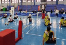 Beyaz ve sarı forma giyen iki takım, oturarak voleybol maçı yapıyor.