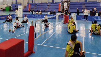 Beyaz ve sarı forma giyen iki takım, oturarak voleybol maçı yapıyor.