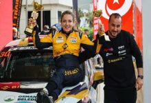 Ralli Pilotu Kübra Denizci Keskin, aracın üstünde oturarak kupaları elinde tutuyor ve yanında erkek bir görevli bulunuyor.