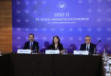 Bir kongre salonunda, üç konuşmacı panel masasında yan yana oturuyor. Arkadaki büyük ekranda "33. Ulusal Neonatoloji Kongresi" yazısı yer alırken, ortam akademik ve resmi bir toplantı atmosferi taşıyor.