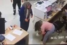 Bir güvenlik kamerası görüntüsünde, hastane benzeri bir ortamda küçük bir çocuğa müdahale eden bir kadın görülüyor. Kadın eğilmiş şekilde çocuğa yardım etmeye çalışırken, çevrede bulunan diğer kişiler durumu endişeyle izliyor. Görüntü, acil bir sağlık müdahalesi anını yansıtıyor.