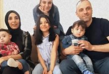 Altı kişilik, samimi bir aile pozu; yetişkinler ve çocuklar koltuk etrafında yakın şekilde oturuyor.