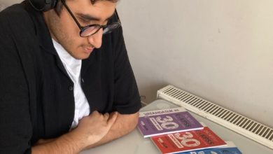 Görme engelli Ömer Miraç Şahin sırada oturuyor ve önünde üç tane EKPSS kitapçığı bulunuyor.
