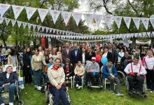 Ağaçlık bir park alanında, üzerlerinde "Hayal Etmek Özgürlüktür" yazılı flamaların asılı olduğu bir meydanda; tekerlekli sandalyedeki bireyler, çocuklar ve yetişkinlerin bir arada olduğu kalabalık bir grup fotoğrafıdır. Sosyal dayanışma temalı bir açık hava etkinliğini yansıtmaktadır.