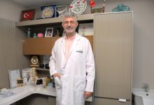 Özel Sağlık Hastanesi Beyin ve Sinir Cerrahisi Uzmanı Op. Dr. Serkan Zengin, çalışma odasında ayakta durmakta ve gülümsemektedir.