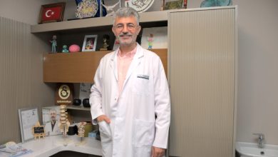 Özel Sağlık Hastanesi Beyin ve Sinir Cerrahisi Uzmanı Op. Dr. Serkan Zengin, çalışma odasında ayakta durmakta ve gülümsemektedir.