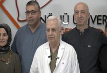 Görselde, bir sağlık kuruluşunda çekilmiş toplu bir fotoğraf yer alıyor. Ön sırada beyaz önlük giyen yaşlı bir doktor bulunurken, arkasında ve yanında sağlık çalışanları görülüyor. Arka planda hastane veya tıp merkezi logosunun bir bölümü yer alıyor. Fotoğraftaki kişiler kameraya dönük şekilde poz veriyor ve görüntü, tıbbi bir başarı ya da basın açıklaması sonrası çekilmiş ekip fotoğrafı izlenimi veriyor.