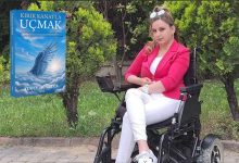 Tekerlekli sandalyesinde oturan genç bir kadın, açık havada yeşillikler arasında poz veriyor. Üzerinde parlak pembe bir blazer, beyaz pantolon ve beyaz ayakkabılar var; güneş gözlüğü başının üzerinde duruyor. Sol tarafta mavi tonlarda bir kitap kapağı yer alıyor: Kırık Kanatla Uçmak. Kapakta bulutlar arasında ışığa doğru yükselen kanatlı bir figür görülüyor.