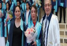 Görselde, mezuniyet töreninde çekilmiş bir an yer alıyor. Ortada mezun cübbesi giymiş genç bir kadın elinde çiçek buketiyle dururken, yanında annesi ve akademik cübbe giymiş bir öğretim üyesi poz veriyor. Arka planda ise törene katılan diğer mezunlar görülüyor.