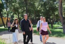 Konyaaltı Belediye Başkanı Cem Kotan ve belediye bürokratları yeşil bir dış alanda incelemelerde bulunurken, kadın eğitmen kendilerine eşlik ediyor.