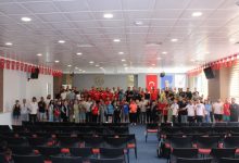 Toplantı salonunda yöneticiler ve sporcular sahnede birlikte anı pozu veriyor.