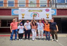 Görselde, okul binasının önünde kupa ve madalyalarıyla poz veren öğrenci ve öğretmenlerden oluşan bir grup görülüyor. Ortadaki öğrenciler kupayı havaya kaldırırken, arka plandaki "Akıl ve Zeka Oyunları Ligi Şampiyonu" yazılı afiş takımın birincilik başarısını vurguluyor. Grup sevinç içinde kameraya poz veriyor.