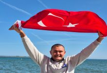 Ultra maraton yüzücüsü Tuna Tunca, Türk Bayrağını havaya kaldırıp poz veriyor.