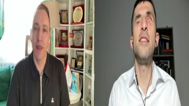 Görselde, YouTube üzerinden gerçekleştirilen çevrim içi programdan alınmış iki konuşmacılı bir ekran görüntüsü yer alıyor. Sol tarafta bir kişi ofis ortamında, arka planda ödül ve plaketlerin bulunduğu rafların önünde konuşurken; sağ tarafta kulaklık kullanan diğer konuşmacı sade bir arka plan önünde programa uzaktan bağlanıyor.