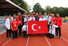 İşitme Engelliler Atletizm Takımı Milli Sporcuları, teknik kadro ile Türkiye İşitme Engelliler Spor Federasyonu Başkanı Dursun Gözel pistte Türk bayrağı tutarak poz veriyor.