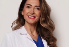Doç. Dr. Ebru Zülfikaroğlu, beyaz hekim önlüğü ve mavi üstüyle profesyonel bir duruş sergileyen, uzun dalgalı kahverengi saçlara sahip bir kadın sağlık profesyoneli olarak görünüyor. Arka planın sade ve açık tonlarda olması, portreyi daha da öne çıkarıyor ve kendisinin uzmanlık alanını yansıtan güven veren bir ifade oluşturuyor.