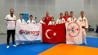 Down Judo Millî Takımı sporcuları ile teknik heyet, Türk Bayrağı, Spor Toto, TÖSSFED flamalarını tutarak spor salonunda poz veriyor.