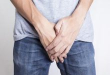 Kot pantolon ve tişört giyimli erkek kişi ağrı olan genital bölgesini eliyle tutuyor.