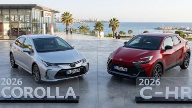 Sahile yakın açık alanda yapılan bir tanıtım alanında Toyota marka iki araç yan yana sergileniyor. Solda gümüş renkli 2026 Corolla, sağda kırmızı 2026 C‑HR bulunuyor. Her iki modelin önünde şeffaf tanıtım panoları yer alıyor ve arka planda palmiye ağaçları ile modern bir Toyota binası görünüyor.