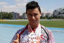 Görselde milli sporcu, atletizm pistinde boynundaki madalyalarıyla poz vererek başparmağını kaldırıyor.