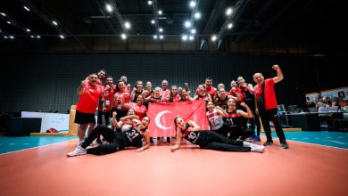 Oturarak Voleybol Kadın Milli Takımı ve teknik heyet, Türk bayrağı tutarak poz veriyor.