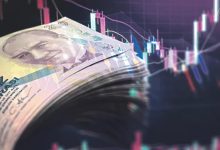 Bir yığın hâlinde duran 200 Türk Lirası banknotları ön planda görülüyor. Arka planda ise dijital finans grafikleri yer alıyor; kırmızı ve yeşil çizgiler, mum grafikleri ve veri noktaları ekonomik hareketliliği simgeliyor. Görsel, Türkiye’de ekonomi ve yatırım trendleri temasını yansıtıyor.