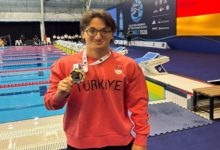 Para Yüzücü Turgut Aslan Yaraman, mercan renkli uzun kollu, Türkiye yazılı tişörtle ve boynunda bulunan madalyayla poz veriyor.
