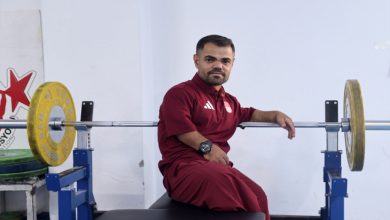 Görselde, spor salonunda ağırlık kaldırma ekipmanlarının yanında oturan, bordo renkli spor kıyafetleri giyen Abdullah Kayapınar bulunuyor.