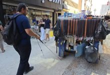 Murat Budak, şehir içinde yürürken beyaz baston kullanan bir birey olarak görülüyor. Önünde seyyar araba var. Seyyar araba tezgâhında kemerler ve çeşitli küçük ürünler sergileniyor. Trafiğe kapalı bir cadde. Resim görme engelli bir bireyin bariyerler nedeniyle bağımsız hareket edemediğini gösteriyor.