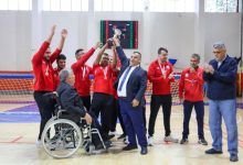 Sporcuların kırmızı formalarıyla kupayı kaldırarak sevinçlerini paylaştığı salonda, takım arkadaşları ve yöneticiler büyük bir coşkuyla şampiyonluğu kutlarken çevredekiler onları alkışlayarak tebrik etmektedir.