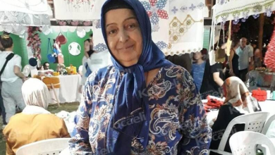 Görselin üst bölümünde, el emeği ürünlerin sergilendiği bir kermes veya pazar yerinde tezgâhının önünde durarak hafifçe gülümseyen engelli pazarcı Durdu Bayrak yer alıyor. Mavi tonlarında desenli bir elbise giyen ve lacivert başörtüsü takmış olan kadının başörtüsünün yakasında okuma gözlüğü asılı duruyor. Çevresinde ve başının üzerinde el işi danteller, işlemeli örtüler ve örgüler sergilenirken; arka planda beyaz plastik sandalyeler, stantları gezen vatandaşlar ve pazar alanının kalabalığı görülüyor.