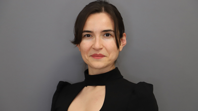 Görselde, sade gri bir arka plan önünde profesyonel bir portre çekimi yapılmış. Elif Türel, koyu renkli, yüksek yakalı ve göğüs kısmında küçük bir kesim detayı bulunan şık bir üst giyiyor. Saçları düzgünce geriye taranmış ve yüz hatlarını net şekilde ortaya çıkaran yumuşak bir ışık kullanılmış. Duruşu dik, ifadesi kendinden emin ve akademik bir profesyonelliği yansıtıyor.