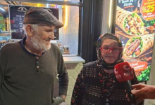 Görselde, bir sokak veya işletme önünde röportaj veren ileri yaşlarda iki kişi yer almaktadır. Sol tarafta kasketli ve sakallı bir erkek ayakta dururken, sağ tarafta ise başörtülü, kırmızı gözlüklü bir kadın ellerinde mikrofonla konuşmaktadır. Arka planda ise bir restorana ait yemek görselleri bulunan ışıklı bir pano görülmektedir.